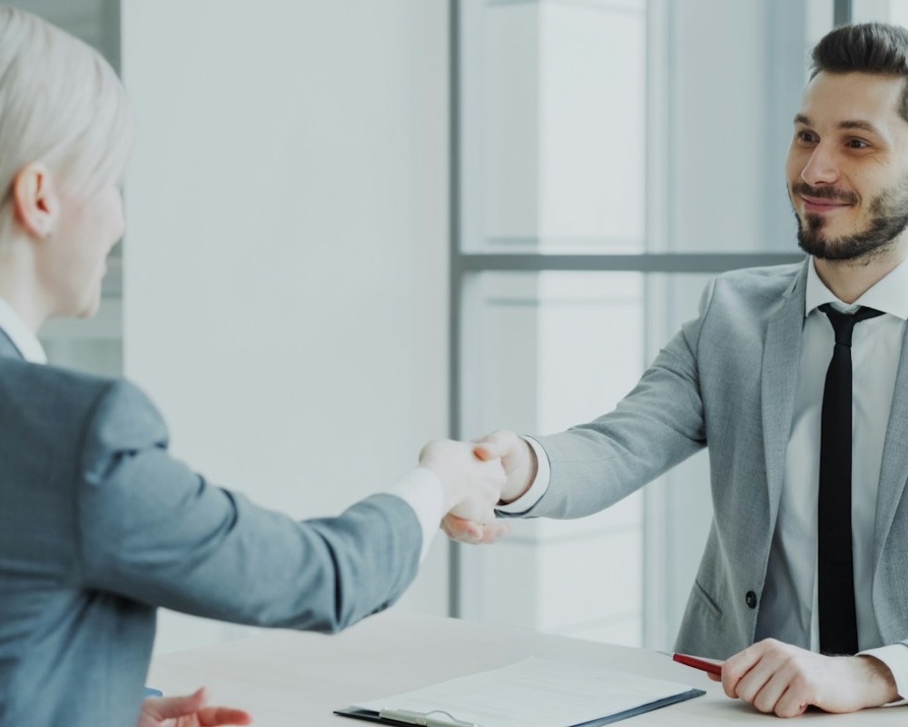 Manager shaking hands with a new employee across a desk
